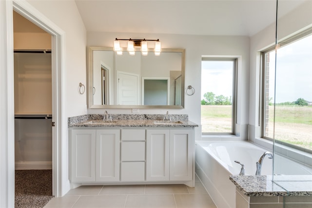 bathroom featuring vanity, vaulted ceiling, tiled tub, and tile patterned flooring