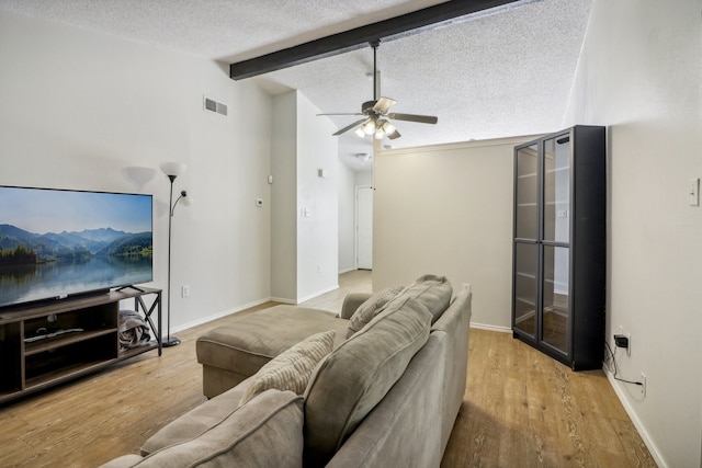 living room featuring light hardwood / wood-style floors, a textured ceiling, vaulted ceiling with beams, and ceiling fan