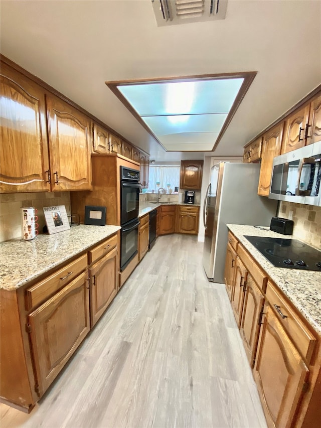 kitchen featuring light hardwood / wood-style floors, tasteful backsplash, black appliances, and sink