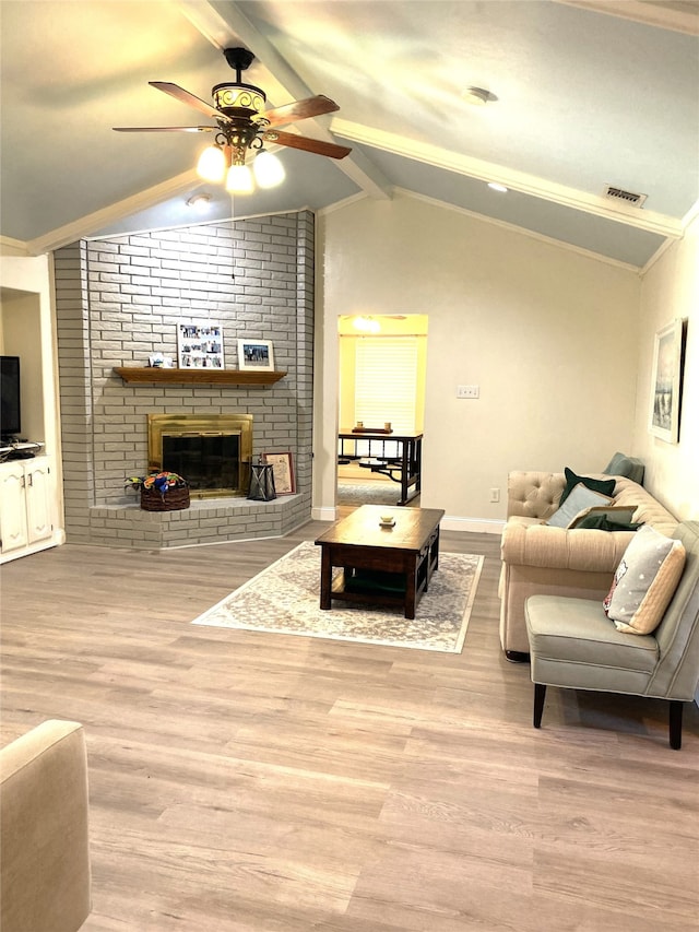 living room featuring lofted ceiling with beams, a brick fireplace, ceiling fan, crown molding, and light hardwood / wood-style flooring