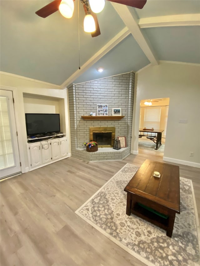 living room featuring light hardwood / wood-style flooring, vaulted ceiling with beams, a brick fireplace, and ceiling fan