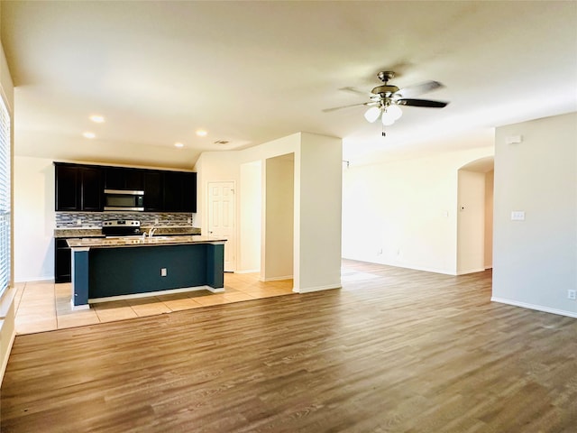 kitchen with an island with sink, stainless steel appliances, light wood-type flooring, and tasteful backsplash