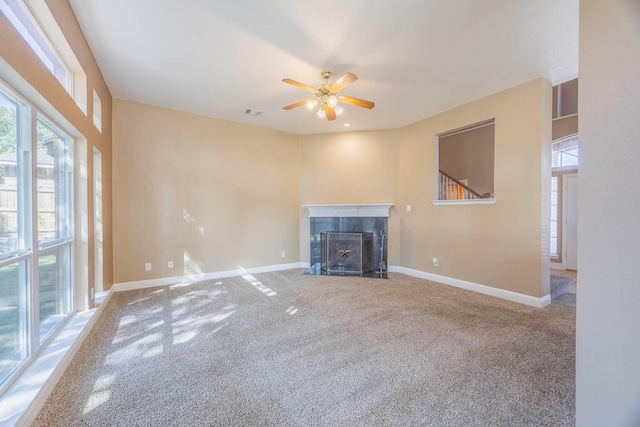 unfurnished living room with a tiled fireplace, carpet floors, and ceiling fan