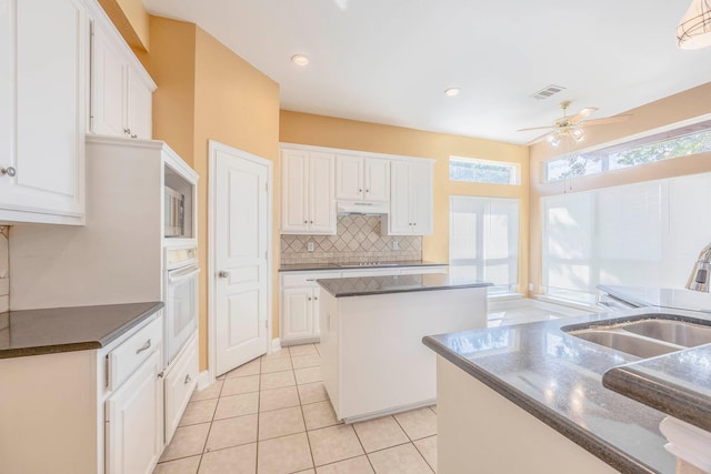 kitchen with oven, white cabinets, backsplash, a center island, and light tile patterned floors