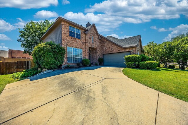 traditional-style home featuring a front lawn, driveway, fence, brick siding, and a garage
