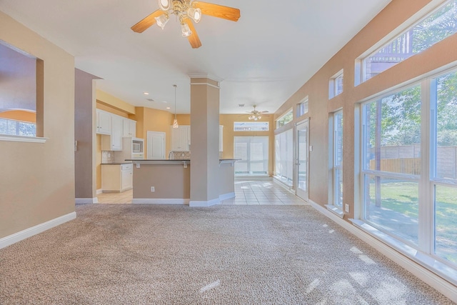 unfurnished living room with a wealth of natural light, light colored carpet, and ceiling fan