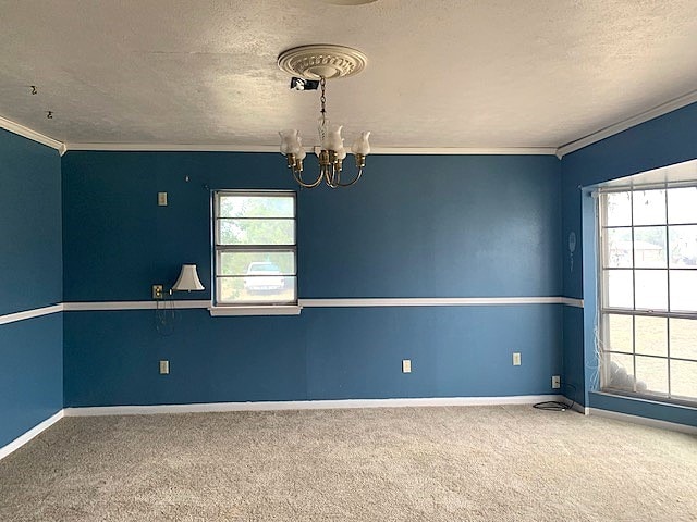807 N Morris Ave, Rotan, TX 79546 - carpeted empty room with a chandelier, a textured ceiling, crown molding, healthy amount of natural light, and baseboards