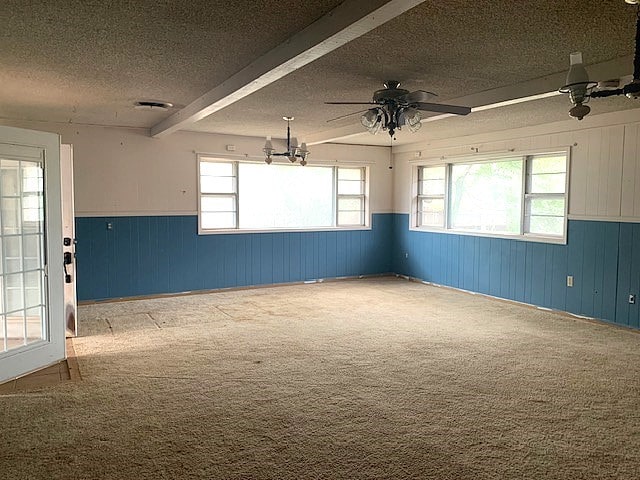 empty room featuring wood walls, a textured ceiling, ceiling fan, beamed ceiling, and light colored carpet