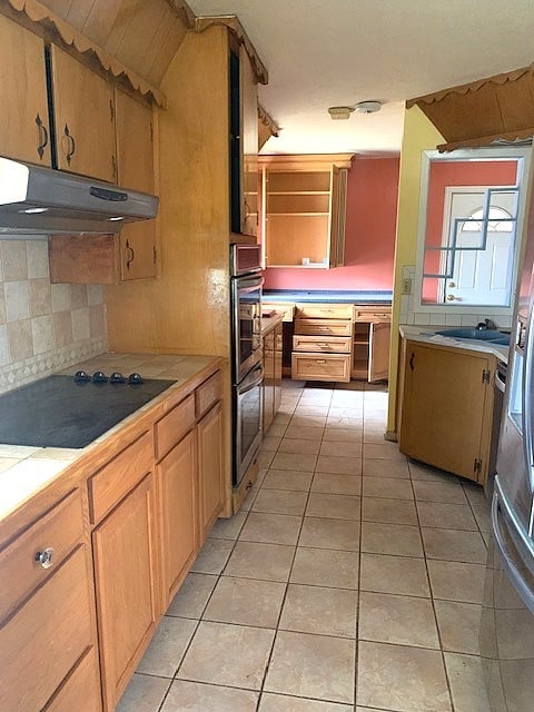 807 N Morris Ave, Rotan, TX 79546 - kitchen with black electric stovetop, under cabinet range hood, tasteful backsplash, stainless steel double oven, and light tile patterned floors