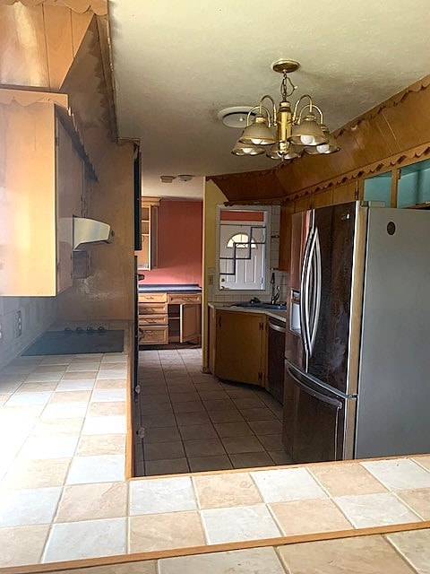 kitchen featuring stainless steel appliances, decorative light fixtures, tile counters, range hood, and a notable chandelier