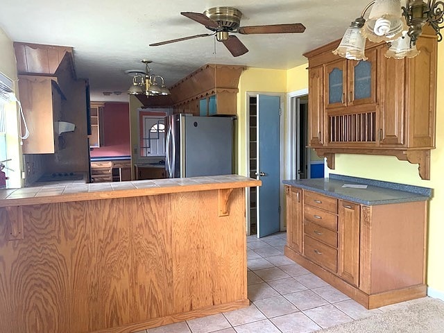 kitchen featuring tile counters, a breakfast bar area, kitchen peninsula, stainless steel fridge, and light tile patterned flooring