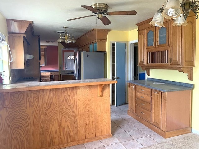 807 N Morris Ave, Rotan, TX 79546 - kitchen featuring freestanding refrigerator, tile counters, glass insert cabinets, and brown cabinetry