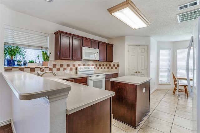 kitchen with white appliances, tasteful backsplash, a kitchen island, kitchen peninsula, and light tile patterned floors