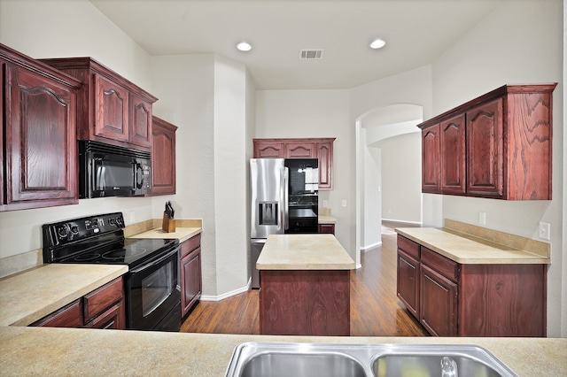 kitchen featuring black appliances, a kitchen island, and dark hardwood / wood-style flooring