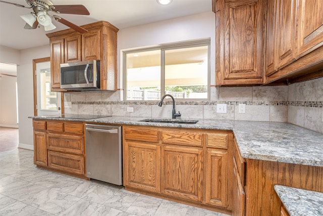 kitchen featuring stainless steel appliances, backsplash, sink, light stone countertops, and ceiling fan