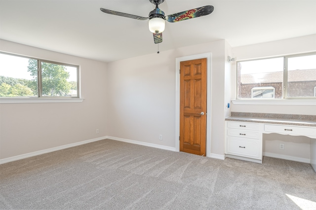 unfurnished bedroom featuring built in desk, ceiling fan, and light carpet