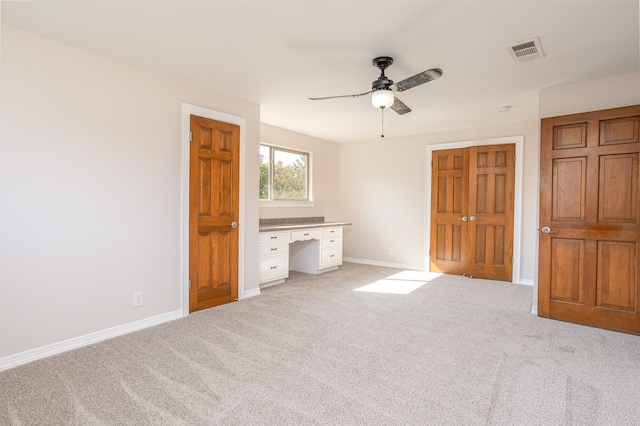 unfurnished bedroom featuring light colored carpet, built in desk, and ceiling fan