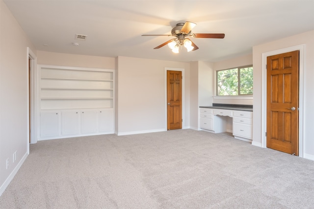 unfurnished bedroom with built in desk, ceiling fan, and light carpet