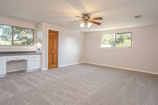 interior space with built in desk, light colored carpet, and ceiling fan