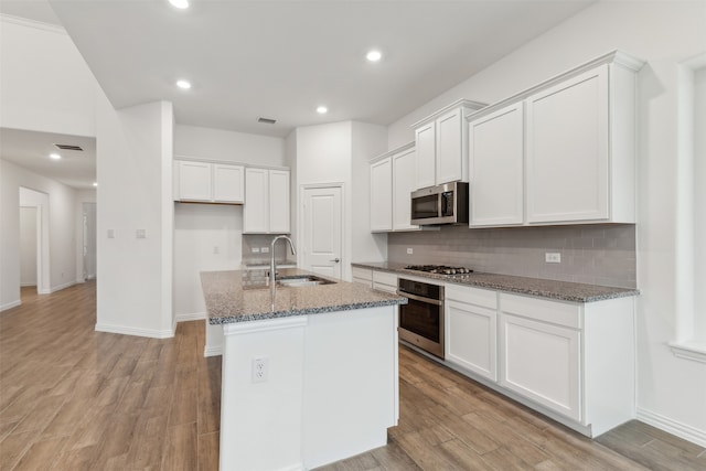 kitchen featuring white cabinetry, appliances with stainless steel finishes, a center island with sink, and dark stone countertops