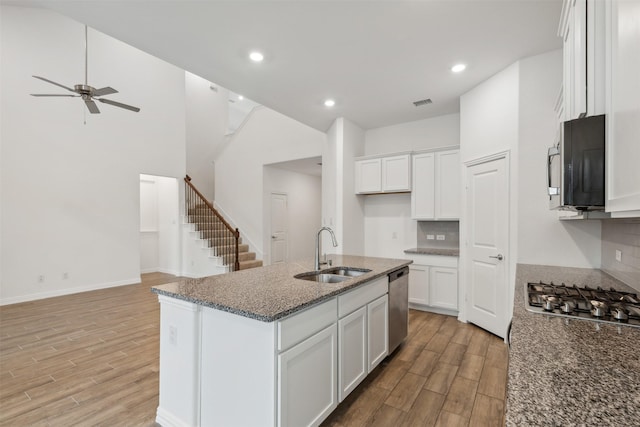 kitchen featuring appliances with stainless steel finishes, white cabinetry, sink, dark stone countertops, and a center island with sink