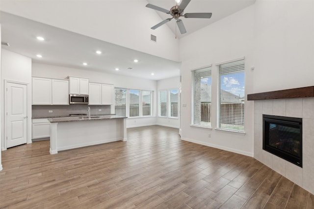 unfurnished living room with sink, light hardwood / wood-style flooring, ceiling fan, a fireplace, and a high ceiling