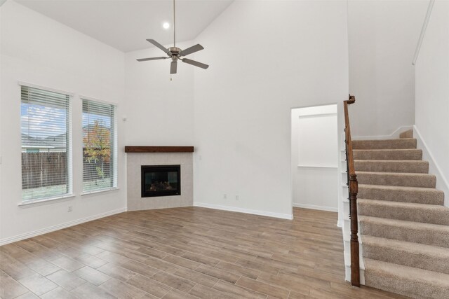 unfurnished living room with a tiled fireplace, high vaulted ceiling, ceiling fan, and light hardwood / wood-style flooring