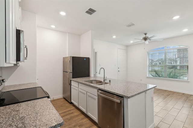 kitchen with sink, white cabinets, stainless steel appliances, light stone countertops, and light hardwood / wood-style flooring