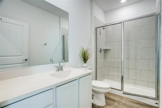 bathroom featuring toilet, vanity, an enclosed shower, and hardwood / wood-style flooring