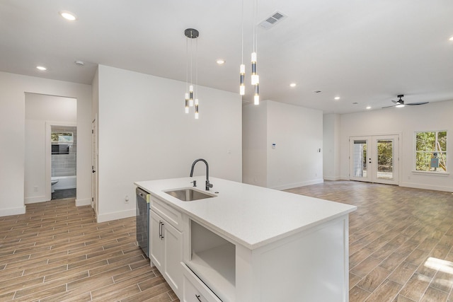 kitchen featuring a center island with sink, open floor plan, hanging light fixtures, white cabinetry, and a sink