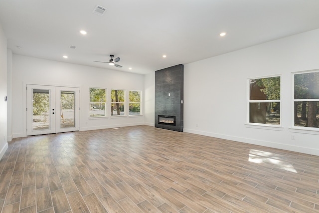 unfurnished living room featuring a fireplace, french doors, light wood-type flooring, and ceiling fan