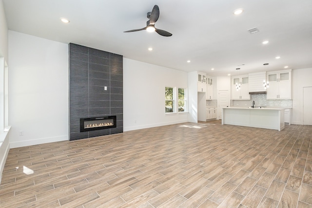 unfurnished living room with light hardwood / wood-style flooring, a tiled fireplace, sink, and ceiling fan