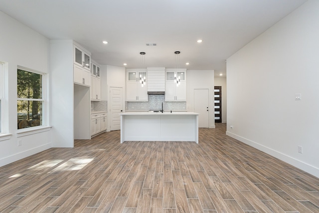 kitchen featuring tasteful backsplash, an island with sink, hanging light fixtures, white cabinetry, and light hardwood / wood-style flooring