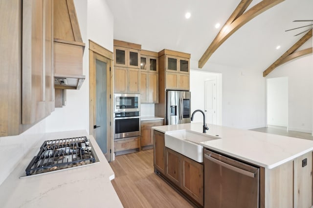 kitchen with sink, appliances with stainless steel finishes, an island with sink, light stone countertops, and light hardwood / wood-style floors