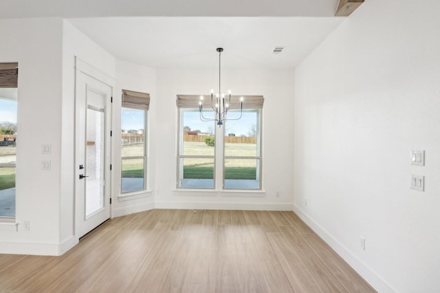 unfurnished dining area featuring an inviting chandelier, a healthy amount of sunlight, and light wood-type flooring