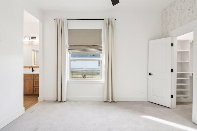 unfurnished bedroom with ensuite bath, ceiling fan, and light colored carpet