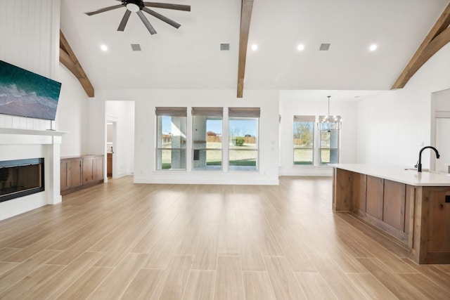 unfurnished living room featuring beamed ceiling, high vaulted ceiling, and ceiling fan with notable chandelier