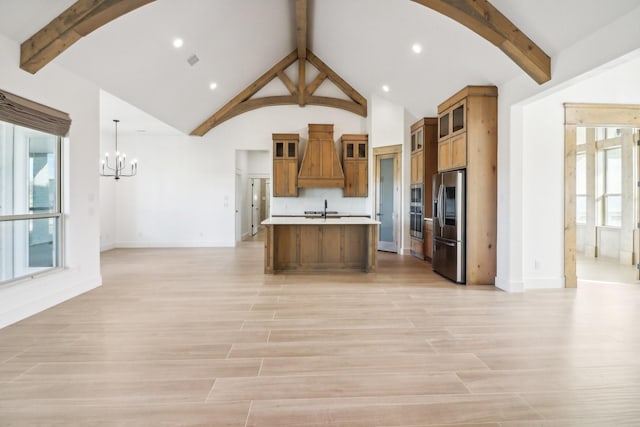 kitchen featuring sink, stainless steel fridge, an island with sink, custom range hood, and pendant lighting