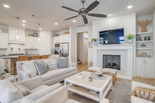 living room featuring light hardwood / wood-style flooring, ceiling fan, sink, and a brick fireplace