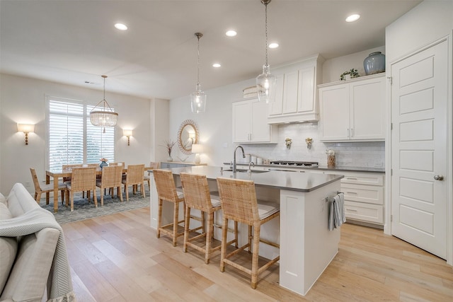 kitchen with a kitchen island with sink, a breakfast bar, pendant lighting, light wood-type flooring, and white cabinetry