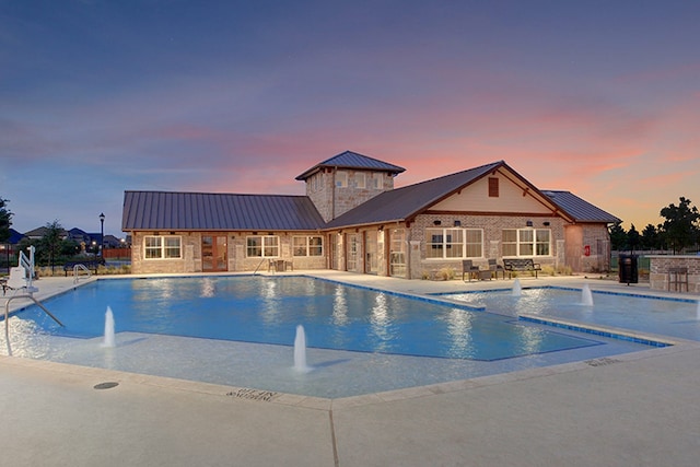 pool at dusk with a patio area and pool water feature