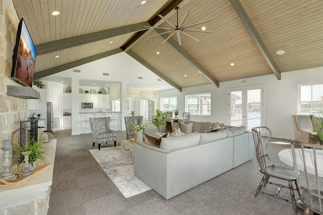 carpeted living room featuring a healthy amount of sunlight, a stone fireplace, high vaulted ceiling, and beam ceiling