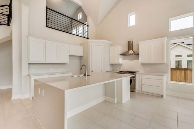 kitchen featuring white cabinets, a center island with sink, high end stove, and wall chimney range hood