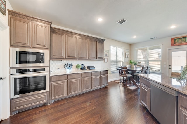 kitchen with appliances with stainless steel finishes, decorative backsplash, light stone countertops, and dark hardwood / wood-style flooring