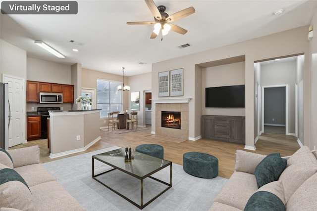 living room with a tile fireplace, ceiling fan with notable chandelier, and light hardwood / wood-style floors