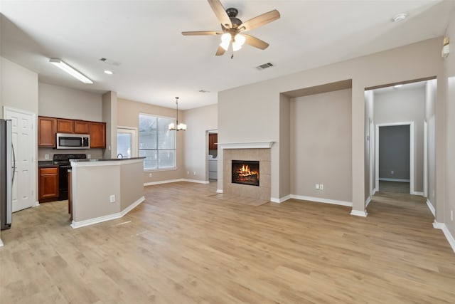 kitchen with a tiled fireplace, light hardwood / wood-style flooring, stainless steel appliances, ceiling fan with notable chandelier, and decorative light fixtures