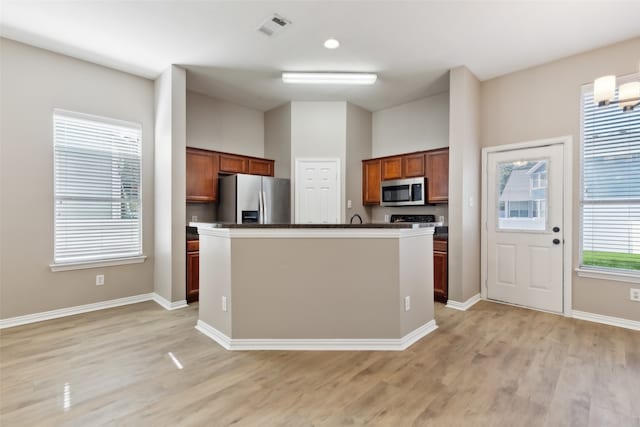 kitchen featuring appliances with stainless steel finishes, an inviting chandelier, a center island with sink, and light hardwood / wood-style floors