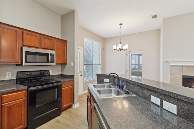 kitchen featuring stainless steel appliances, sink, an inviting chandelier, light wood-type flooring, and a fireplace