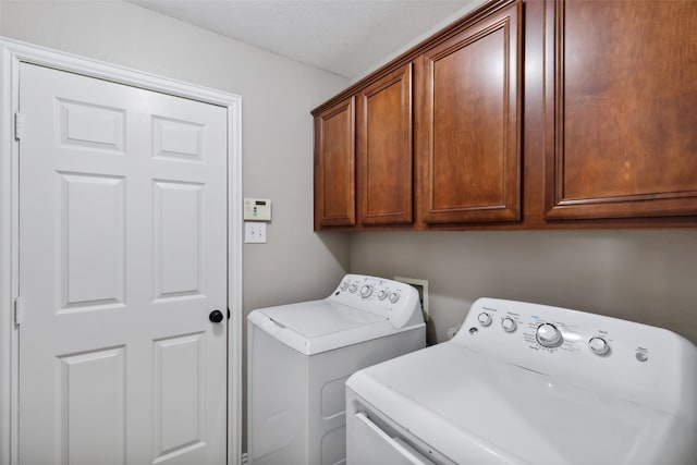 clothes washing area featuring washer and dryer, a textured ceiling, and cabinets