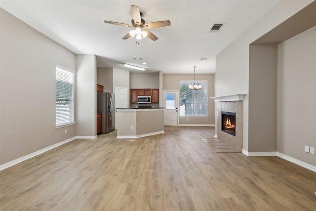 unfurnished living room with light wood-type flooring, ceiling fan with notable chandelier, and a tile fireplace